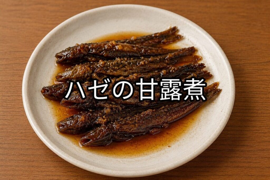 木目調のテーブルの上に置かれた白い丸皿に、細めのハゼの甘露煮を複数盛り付けた和風料理の写真