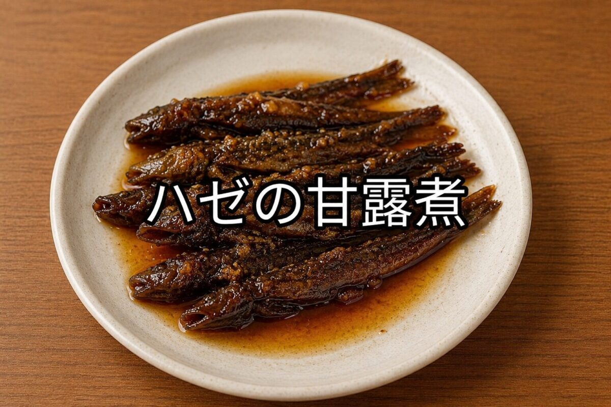 木目調のテーブルの上に置かれた白い丸皿に、細めのハゼの甘露煮を複数盛り付けた和風料理の写真