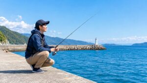青空の下、海沿いの堤防で釣りを楽しむ男性の画像