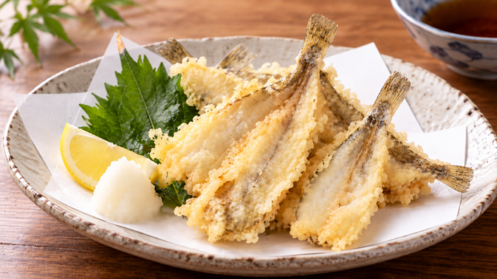 背開きにしたハゼを薄い衣でふっくら揚げ、大葉の天ぷら、レモン、大根おろしと盛り付けた料理写真
