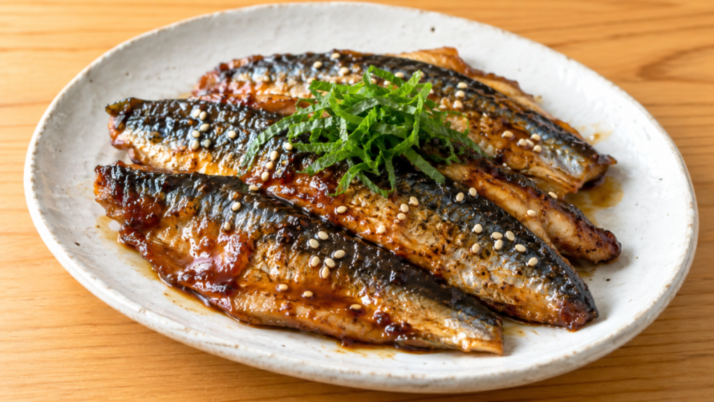 開いたイワシを甘辛いタレで香ばしく焼き、大葉と白ごまを添えた蒲焼きの料理写真