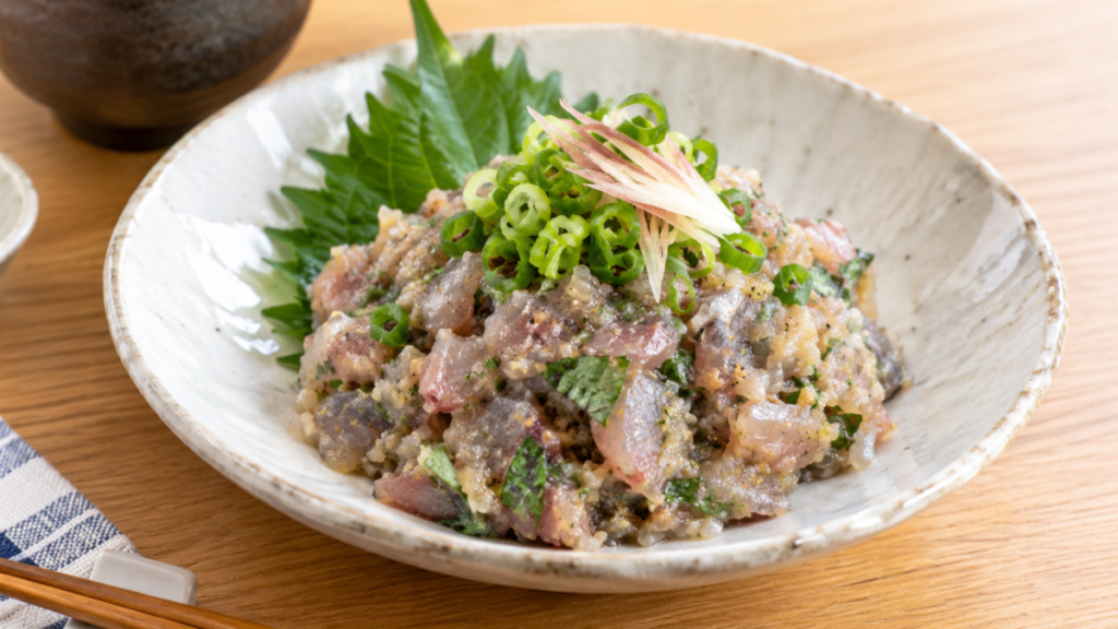 粗くたたいたイワシを味噌と薬味で和え、大葉、青ねぎ、みょうがと盛り付けたなめろうの料理写真