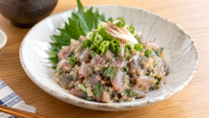 粗くたたいたイワシを味噌と薬味で和え、大葉、青ねぎ、みょうがと盛り付けたなめろうの料理写真
