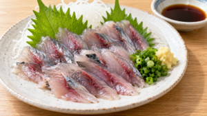 イワシの刺身を大葉、大根のつま、青ねぎ、しょうがと盛り付けた料理写真