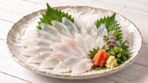 薄くそぎ切りにしたカワハギの刺身を大葉と大根のつま、薬味と盛り付けた料理写真