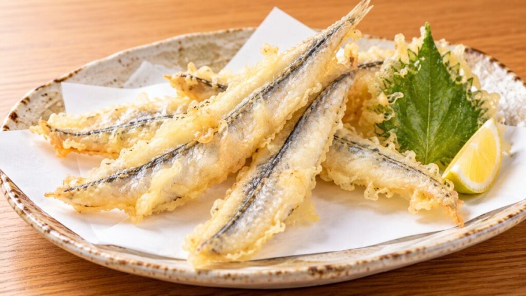 開いたサヨリを薄い衣で揚げ、大葉の天ぷらやレモンと盛り付けた料理写真